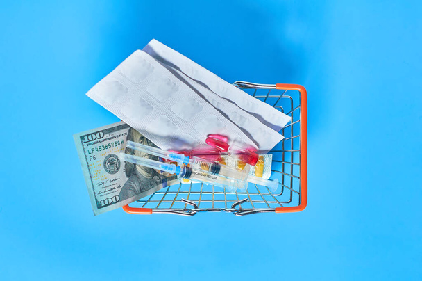 Market basket full of medicaments and banknote of 100 dollars on blue background. Healthcare concept - Фото, зображення