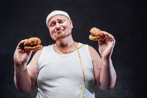 Hombre muy gordo con dos hamburguesas en las manos con los ojos cerrados
 - Foto, Imagen