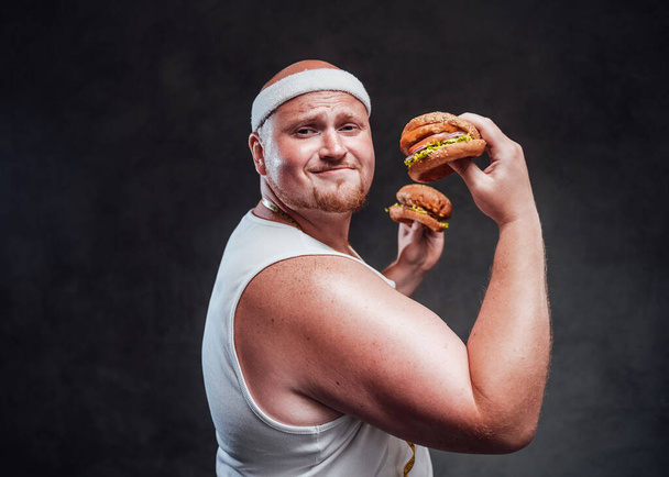  hubby but strong men pulling a face with two hamburgers in his hands - Fotografie, Obrázek
