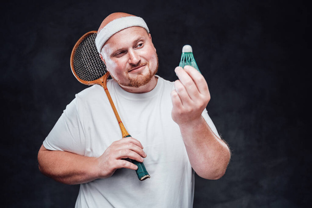 Un sportif chauve avec une fusée de badminton à la main regarde une navette - Photo, image