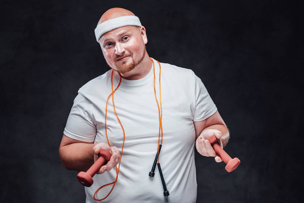 Bulky man in a white T-shirt with two dumbbells in each hand and a rope hanging around his neck - Foto, immagini