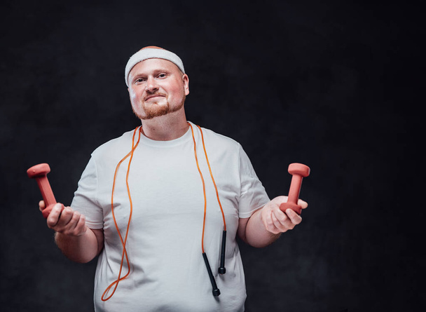 Tubby men with two dumbbells in each hand and a bright orange rope hanging from his neck - Photo, Image