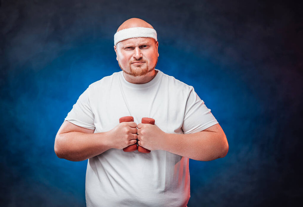 Lihava mies, jolla on kaksi käsipainoa molemmissa käsissä - Valokuva, kuva