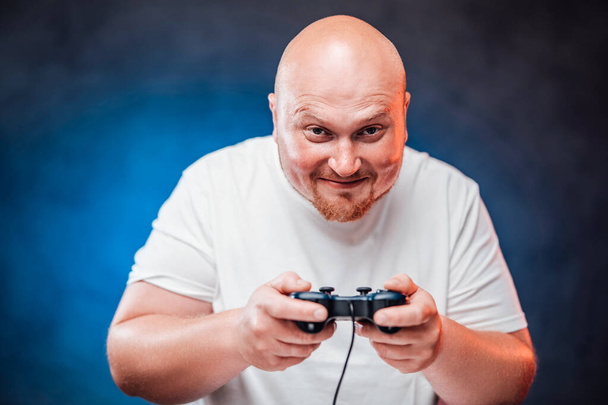  смердючий чоловік у білій футболці грає в ігрову консоль, посміхаючись
 - Фото, зображення