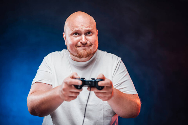Homem robusto em uma camiseta branca joga um console de jogo em estresse
 - Foto, Imagem