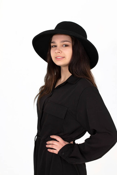 A girl in a black hat poses and smiles on a white background holding her hat - Foto, immagini