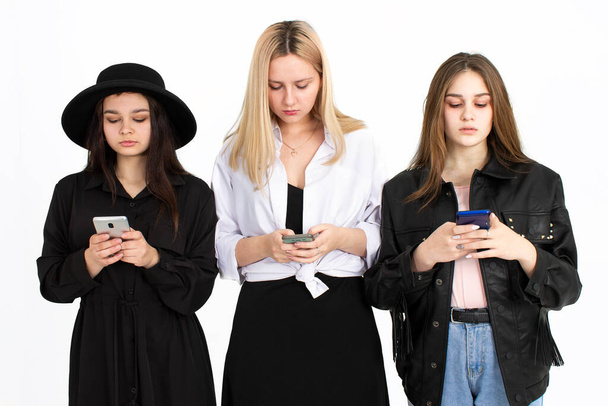 Three young beautiful girls are looking at their smartphones. Photo on a white background - Fotografie, Obrázek