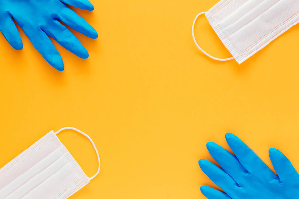 Stock photo of two face masks and two blue gloves on a yellow background and copyspace in the center of the image - Zdjęcie, obraz
