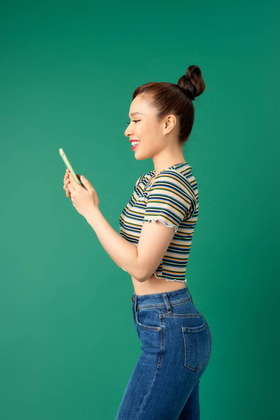 Smiling young Asian girl using smart phone isolated over green background. - 写真・画像