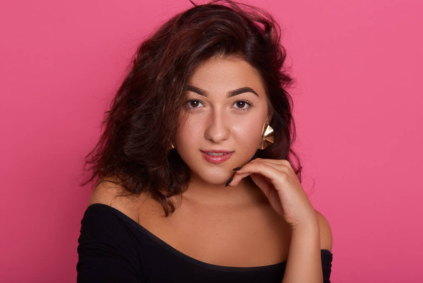 Beautiful woman with wavy brunette hair and clean skin with natural makeup posing with hands under chin against pink background, looking at camera with confident expression. - Fotó, kép