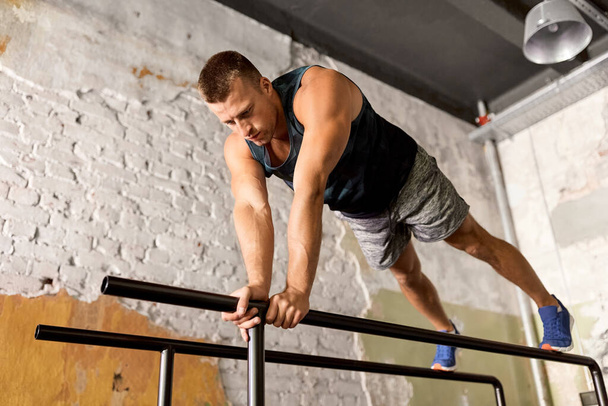 hombre haciendo flexiones en barras paralelas en el gimnasio - Foto, imagen