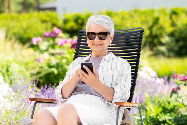 old woman with earphones and smartphone at garden - Photo, image