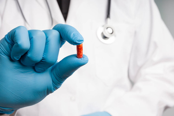 close up da mão do médico em luvas médicas apresentando uma cápsula de medicamento vermelho
 - Foto, Imagem