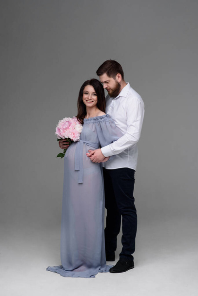妊娠中の女性と彼女の夫は、スタジオで灰色の背景に抱きついています. - 写真・画像