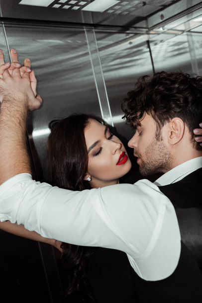 Handsome man kissing beautiful woman with red lips in elevator - Photo, Image