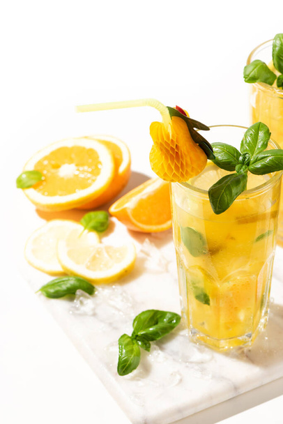 Limonata di agrumi o cocktail di mojito con limone e arancia e basilico. Bevanda fredda o bevanda con ghiaccio sul tagliere di marmo - Foto, immagini