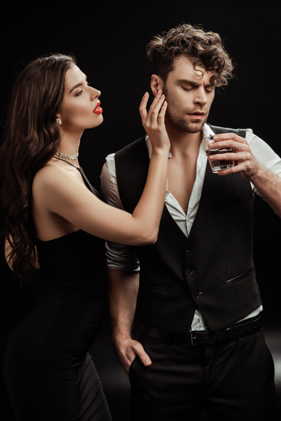 Sexy woman touching boyfriend with glass of whiskey on black  - Fotografie, Obrázek