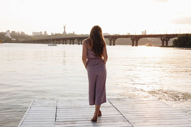 Back view of young woman with beautiful long hair standing on the pier - Foto, Imagem