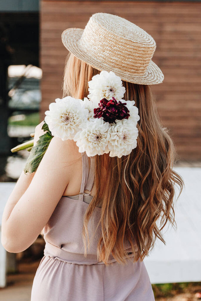 Back view of young woman with beautiful long hair wearing straw hat with flowers - Foto, afbeelding