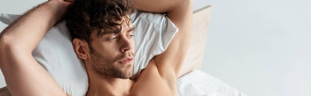 Οριζόντια εικόνα του όμορφου άνδρα χωρίς πουκάμισο ξαπλωμένος στο κρεβάτι απομονωμένος στο λευκό - Φωτογραφία, εικόνα