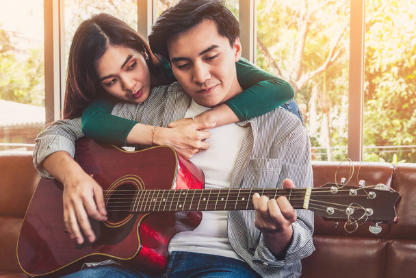 Młoda azjatycka para gra na gitarze i śpiewa piosenkę w salonie w domu razem. Koncepcja muzyki i stylu życia. - Zdjęcie, obraz
