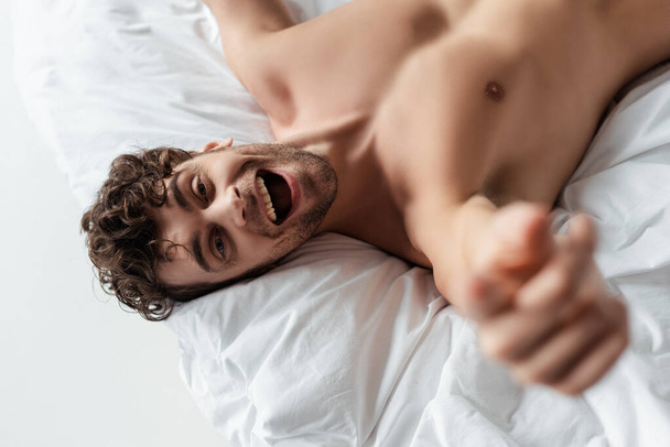 Selective focus of cheerful shirtless man pulling hand at camera isolated on white - Foto, imagen
