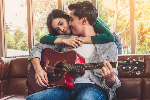 Nuori aasialainen pari soittaa kitaraa ja laulaa laulua olohuoneessa kotona yhdessä. Musiikki ja elämäntapa käsite. - Valokuva, kuva