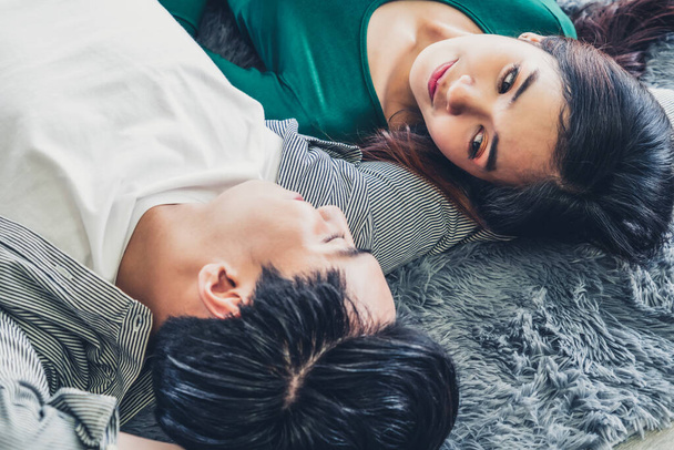 Glückliches asiatisches Paar, das zusammen auf dem Teppich im Wohnzimmer liegt. Liebesbeziehung und Lebensstil-Konzept. - Foto, Bild