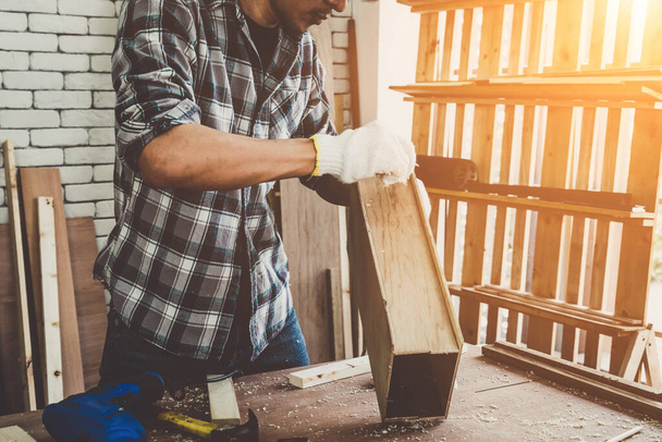 Carpintero trabajando en artesanía de madera en el taller para producir material de construcción o muebles de madera. El joven carpintero asiático utiliza herramientas profesionales para la elaboración. Fabricante de bricolaje y carpintería concepto de trabajo. - Foto, imagen
