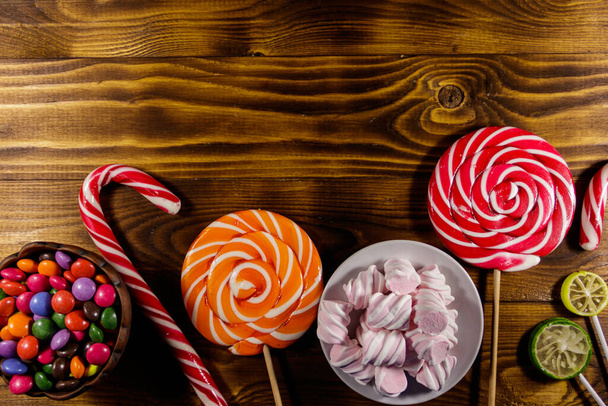 Барвисті шоколадні цукерки, льодяники, цукерки тростина і зефір на дерев'яному столі
 - Фото, зображення