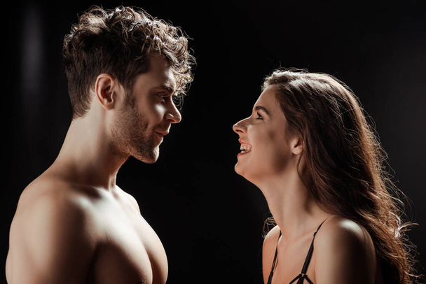Smiling woman looking at shirtless man on black background - Foto, Imagem