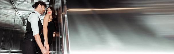 Panoramische oriëntatie van knappe man aanraken sexy vrouw in lift  - Foto, afbeelding