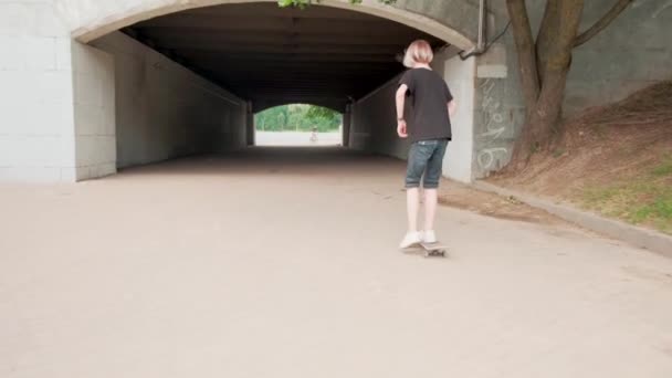 A boy enters a dark tunnel and rides out into the light on a skateboard. - Felvétel, videó