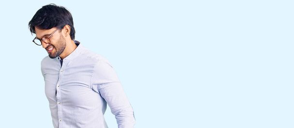 Przystojny Hiszpan w koszuli biznesowej i okularach cierpiący na bóle pleców, dotykający pleców dłonią, ból mięśni  - Zdjęcie, obraz