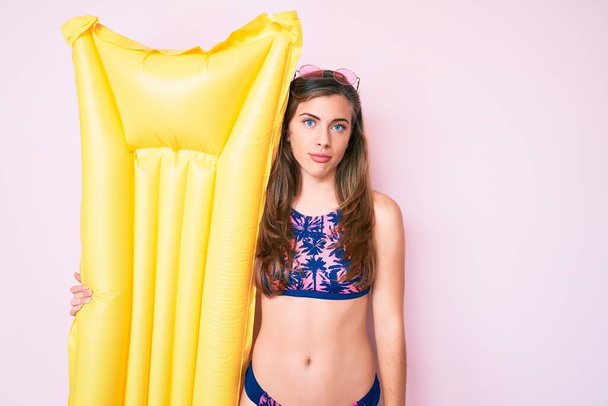Bella giovane donna caucasica indossando bikini e tenendo estate matress galleggiante pensiero atteggiamento e sobria espressione guardando fiducioso di sé  - Foto, immagini