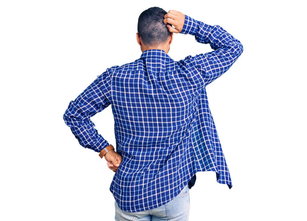 Junger hispanischer Mann in lässiger Kleidung denkt mit der Hand auf dem Kopf rückwärts an den Zweifel  - Foto, Bild