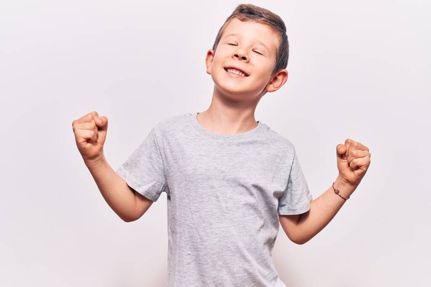 Cute blond kid wearing casual clothes very happy and excited doing winner gesture with arms raised, smiling and screaming for success. celebration concept.  - Fotoğraf, Görsel
