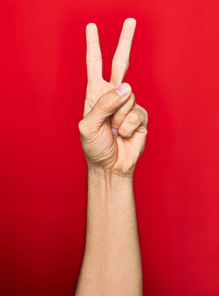 Beautiful hand of man showing two fingers up doing victory sign over isolated red background - Photo, Image