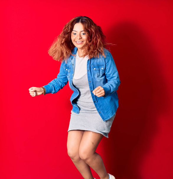若い美しいラテン語の女性が幸せな笑顔カジュアルな服を着て。顔に笑顔でジャンプします勝者ジェスチャーを行います最初とともに上の隔離された赤の背景 - 写真・画像