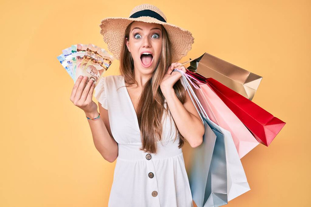 Junge blonde Mädchen mit Einkaufstaschen und kanadischen Dollars feiern verrückt und erstaunt für den Erfolg mit offenen Augen schreien aufgeregt.  - Foto, Bild