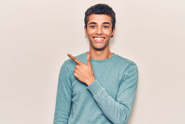 Fiatal afro-amerikai férfi alkalmi ruhát visel mosolygós vidám mutató kéz és ujj fel az oldalra  - Fotó, kép