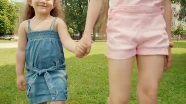 Two beautiful girls sisters are walking on the green grass holding hands. - Video