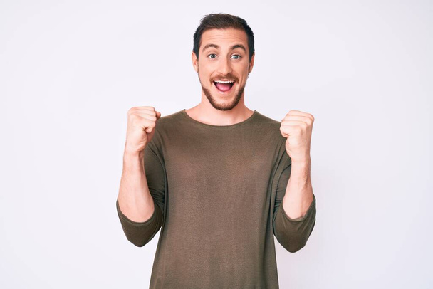 Young handsome man wearing casual clothes celebrating surprised and amazed for success with arms raised and open eyes. winner concept.  - Fotoğraf, Görsel