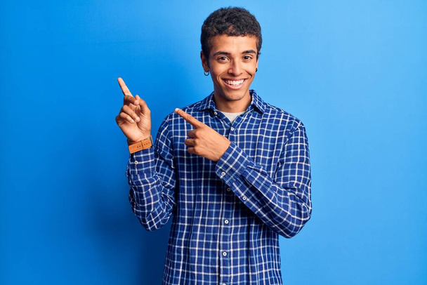 カジュアルな服を着た若いアフリカ系アメリカ人の男が笑顔でカメラを見て両手と指を横に向けて.  - 写真・画像