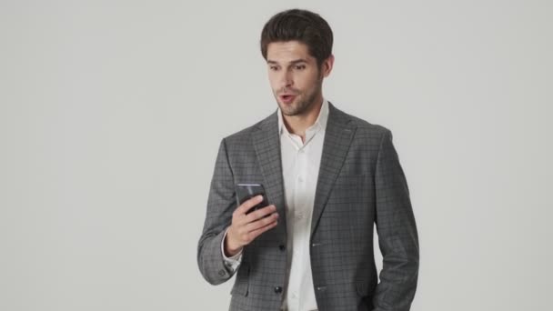 Shocked emotional young business man isolated over white wall while talking by mobile phone - Filmati, video