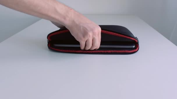 Un homme met un ordinateur portable dans une valise, le referme et enlève la table. L'action. Gros plan de la main masculine plaçant l'ordinateur portable moderne dans les ordures et l'emportant. - Séquence, vidéo