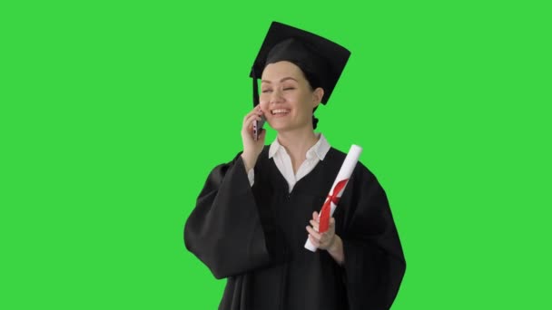 Emotional female student in graduation robe talking on the phone holding diploma on a Green Screen, Chroma Key. - Video