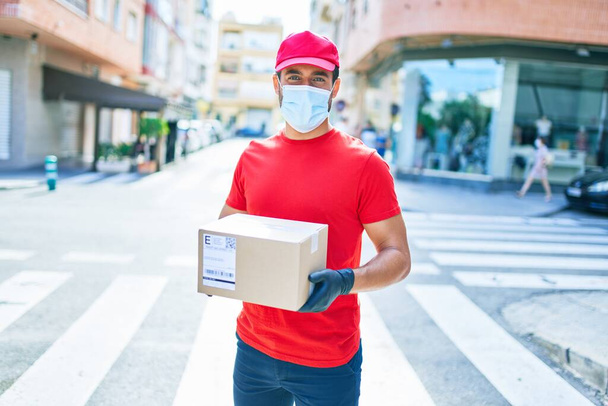 制服を着た若い配達人と町の通りで段ボールパックを保持コロナウイルス保護医療用マスク. - 写真・画像