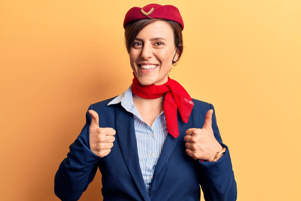 Young beautiful woman wearing stewardess uniform success sign doing positive gesture with hand, thumbs up smiling and happy. cheerful expression and winner gesture.  - Fotografie, Obrázek