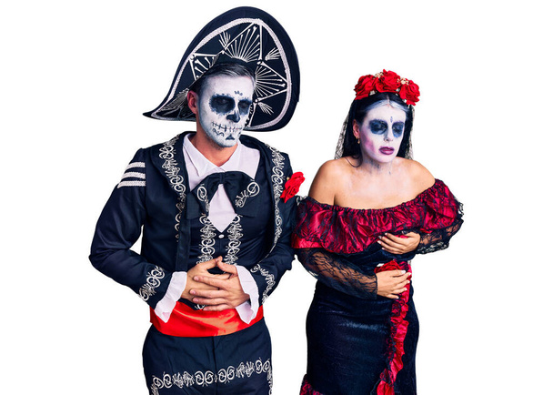 Junges Paar im mexikanischen Totenkostüm über dem Hintergrund mit der Hand auf dem Bauch wegen Verdauungsstörungen, schmerzhafter Krankheit, die sich unwohl anfühlt. Schmerzkonzept.  - Foto, Bild